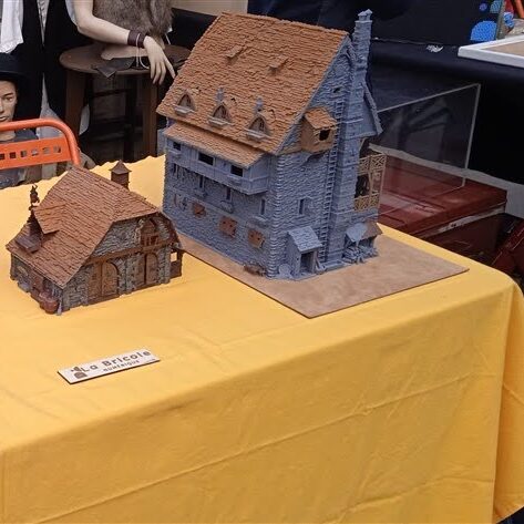 Maquettes de bâtiments imprimés en PLA montrant des façades texturées en pierre et des éléments en bois comme volets, auvents, fenêtres, toits et structures.